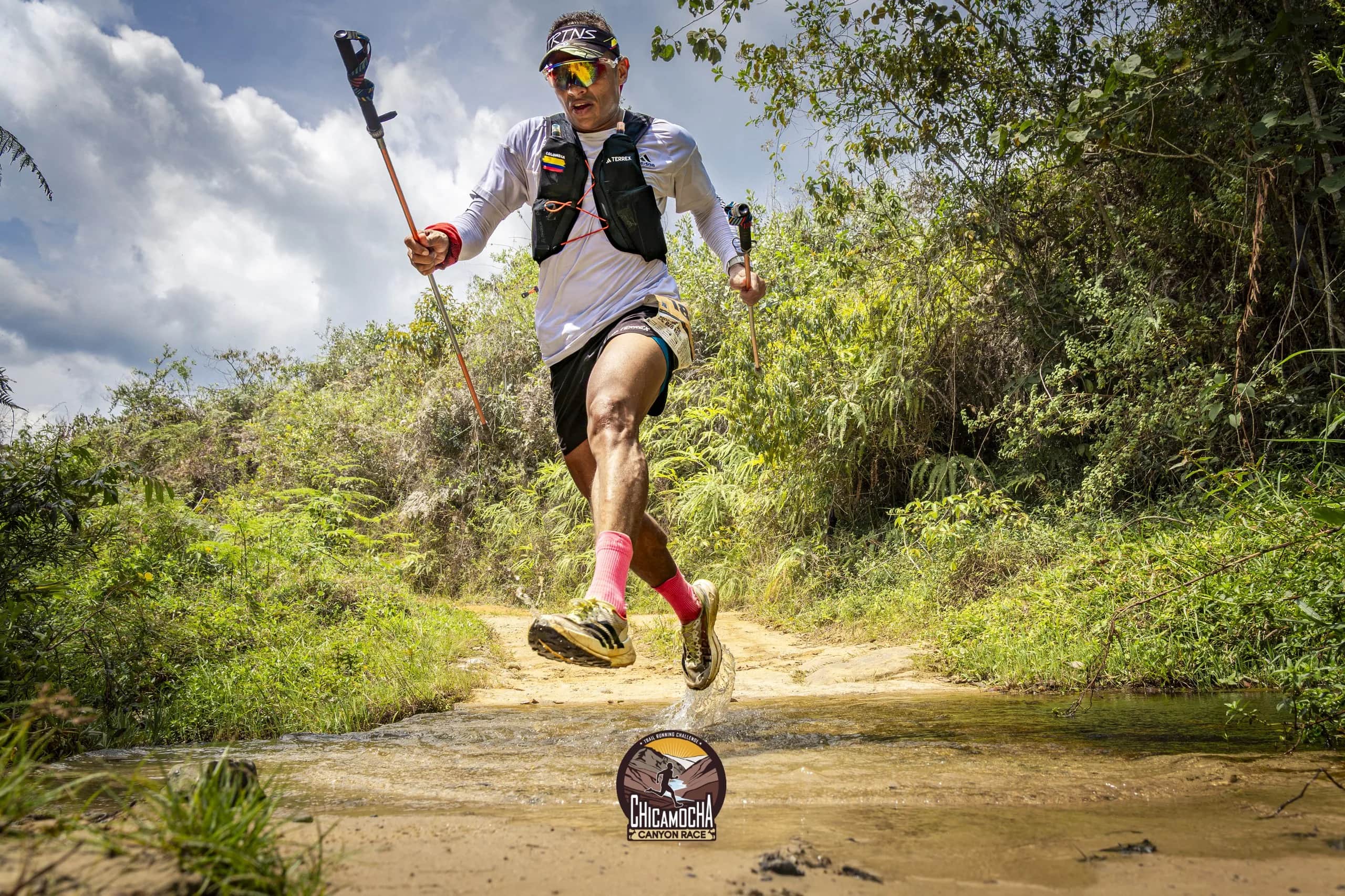 Runner with poles leaping over a stream on a forest trail