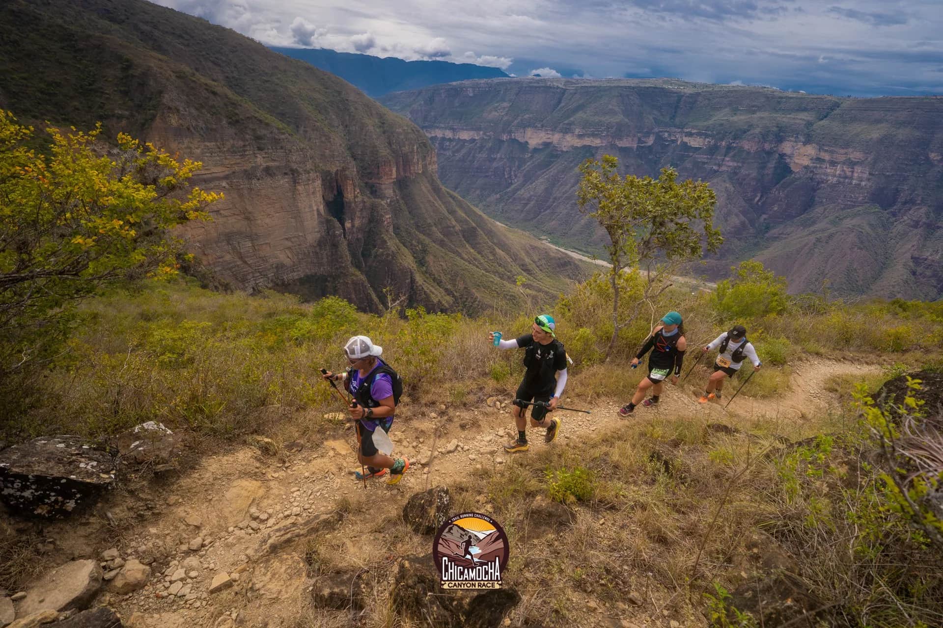 Cuatro corredores suben en fila por un sendero en el borde del cañón