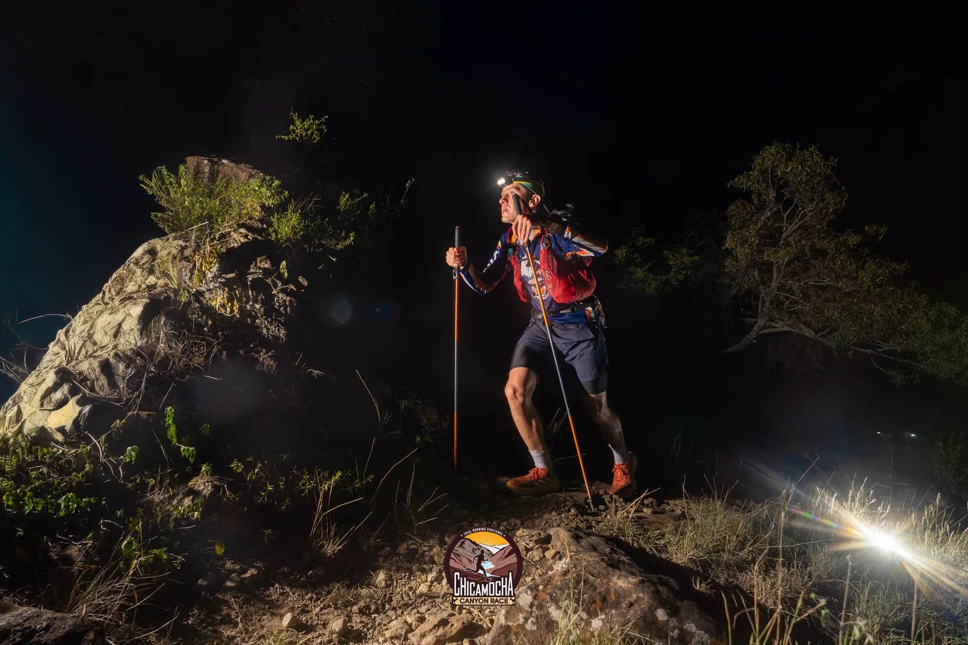 Corredor con linterna frontal y bastones sobre una roca, de noche