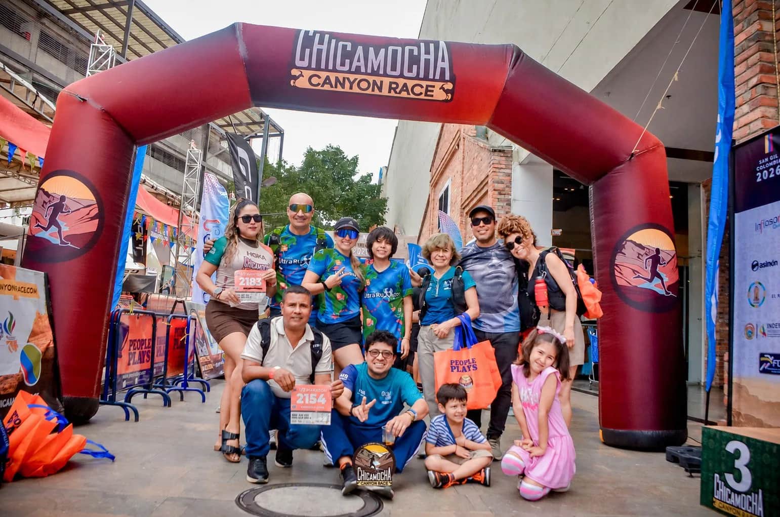 A family of runners poses with their bibs in front of the race arch