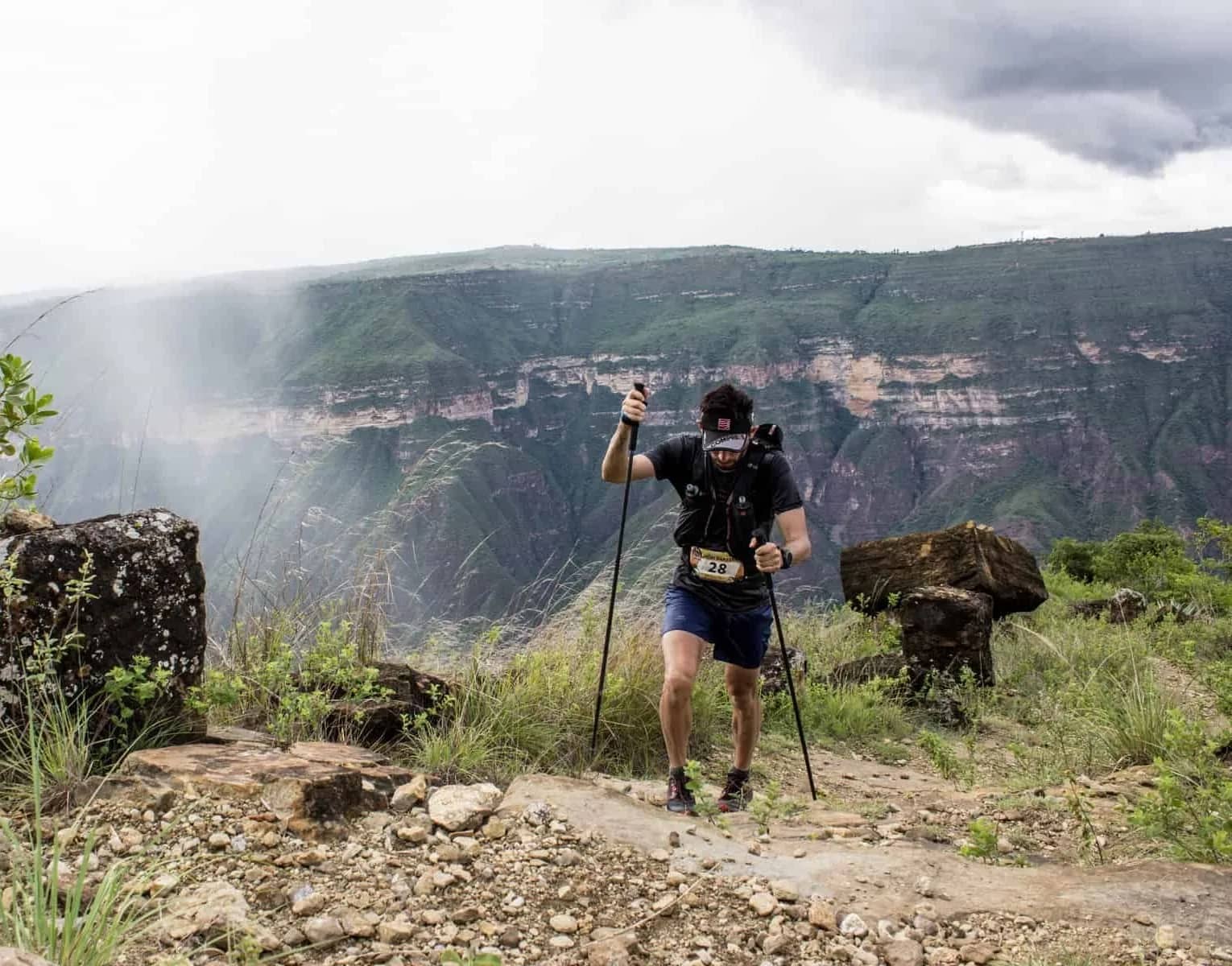 Runner with poles on the rim of the Chicamocha Canyon, with mist-covered canyon walls behind him