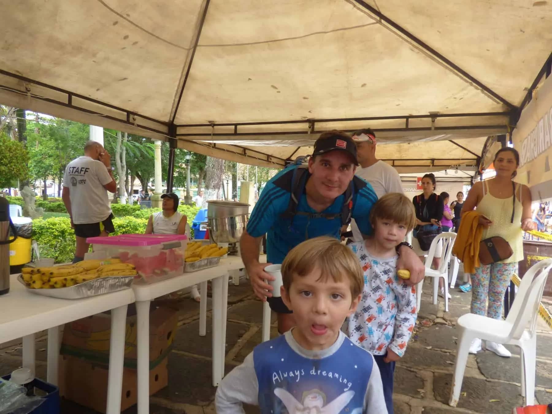 A runner with two children next to the aid-station table of a checkpoint, under a tent