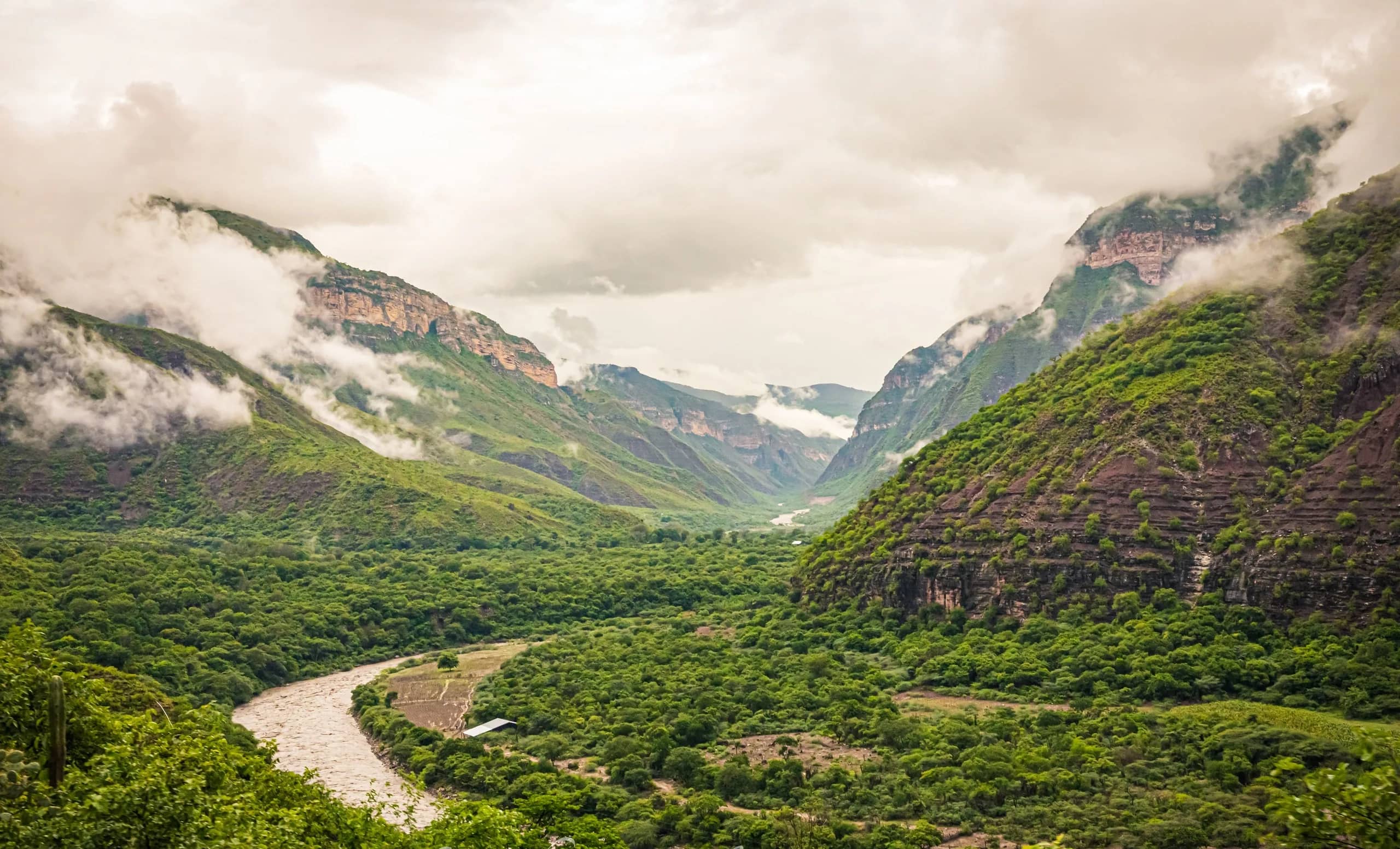 The Chicamocha River winding between green mountains and cloud-covered rock walls