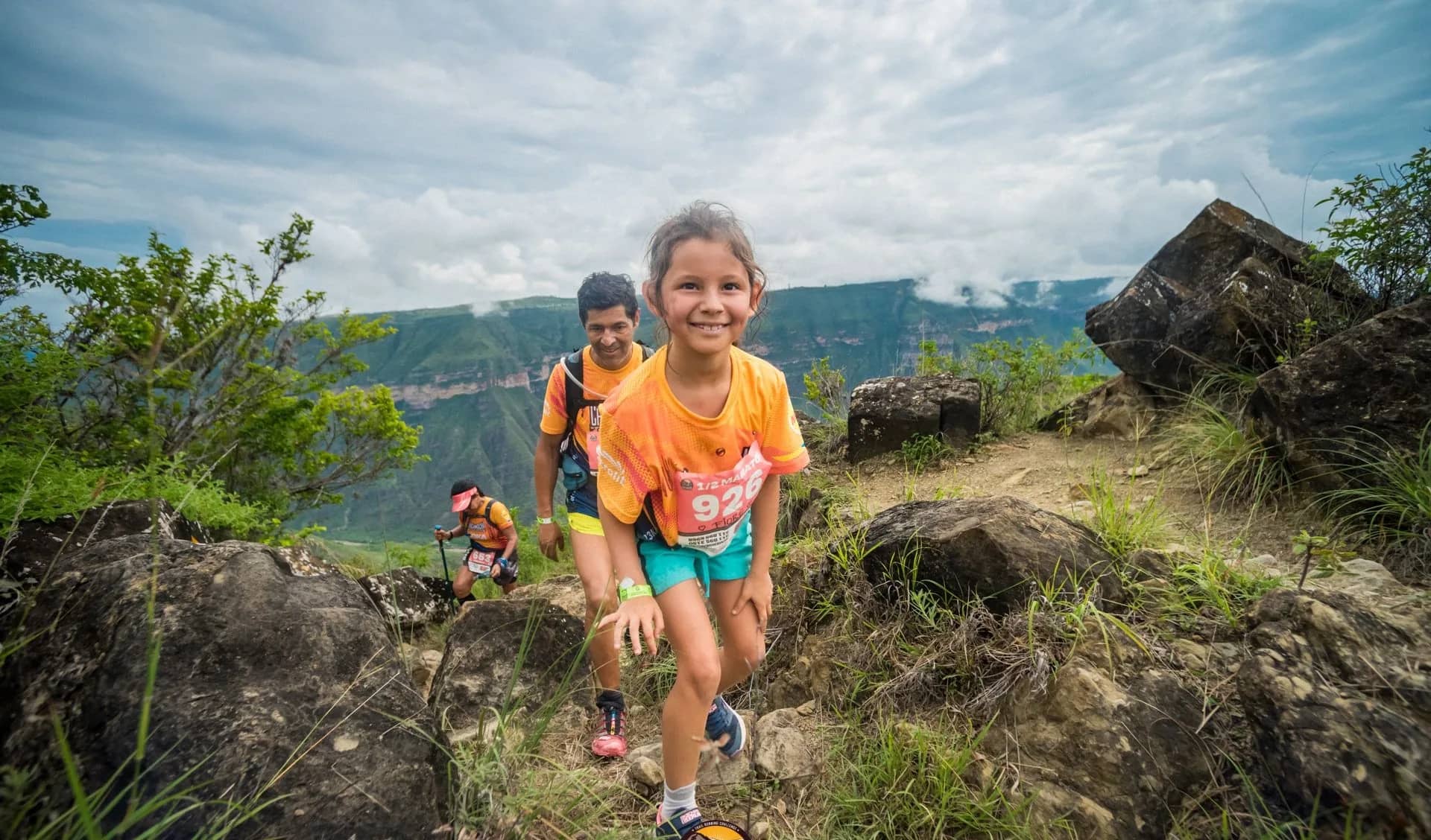 Smiling girl climbing a rocky trail with her family, the canyon behind
