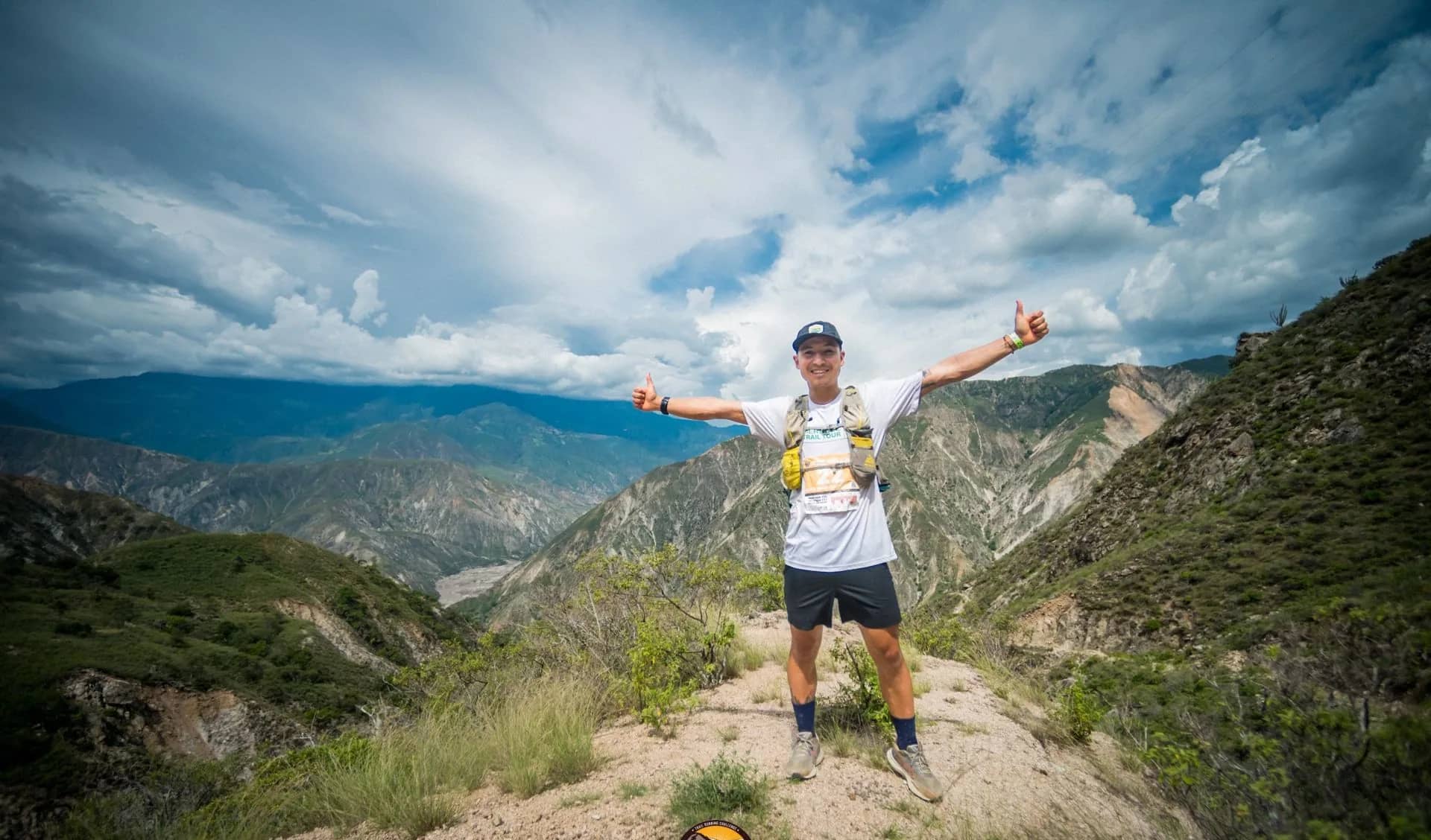 Runner with open arms at the top of a trail, the canyon behind him