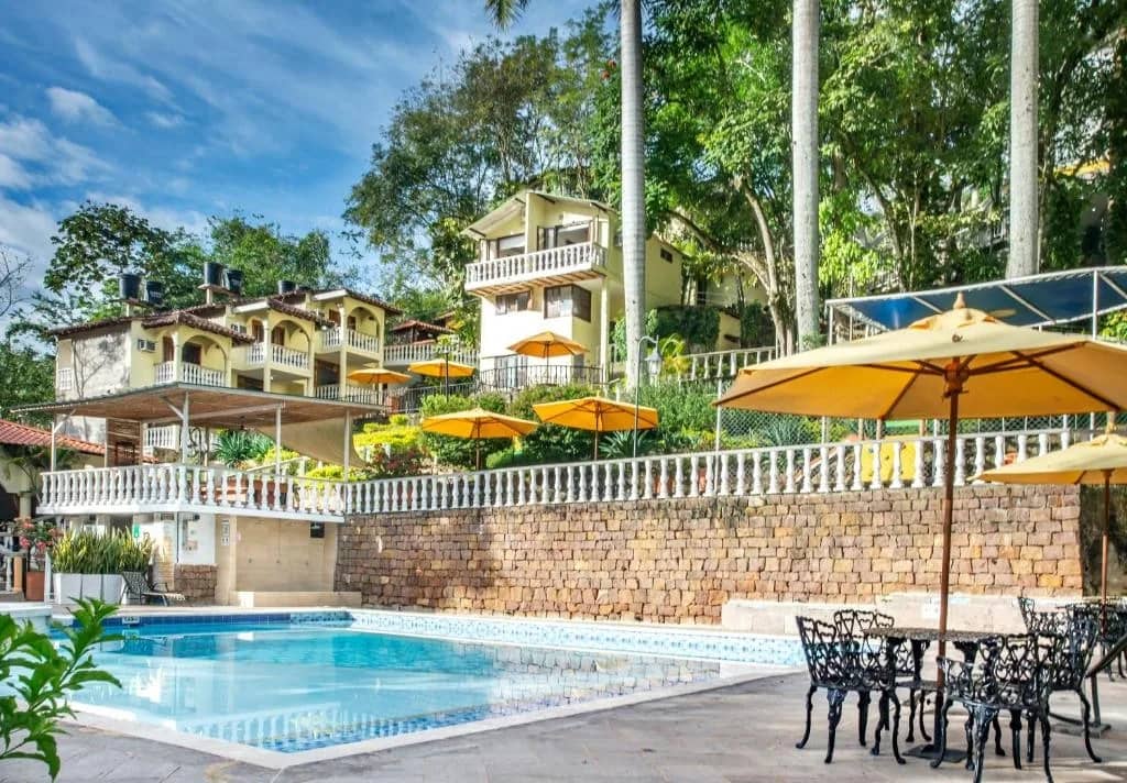 Pool with yellow umbrellas surrounded by gardens at Hotel Posada Campestre