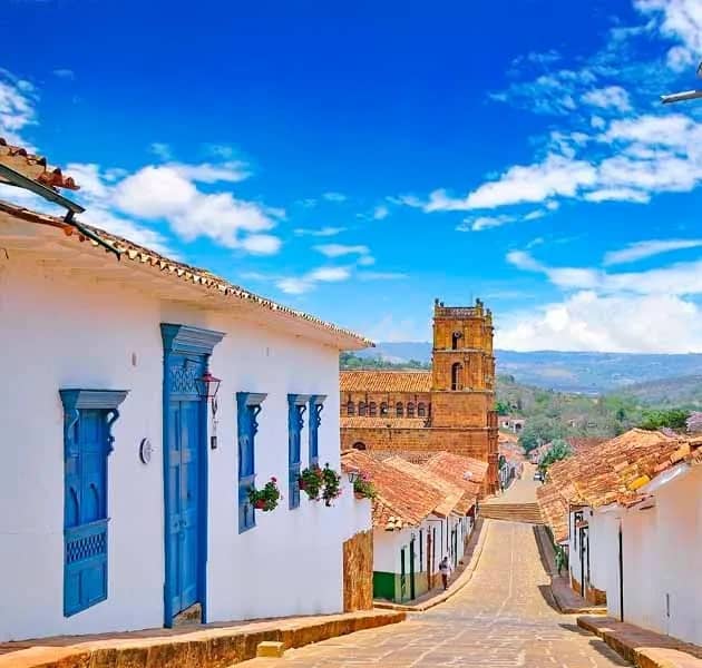 Steep street in Barichara with whitewashed houses, blue doors and the church tower behind