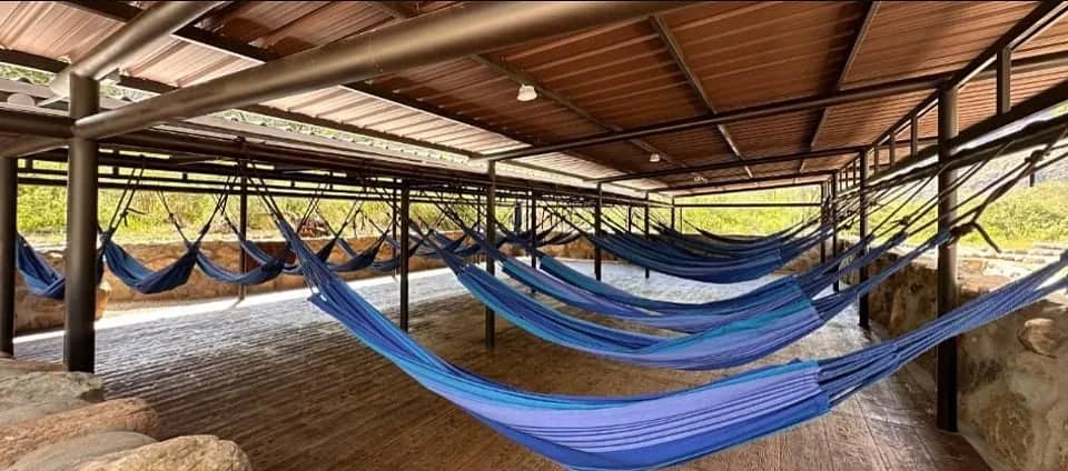 Covered area with rows of blue hammocks at Chicamocha Lodge, among rocks and greenery