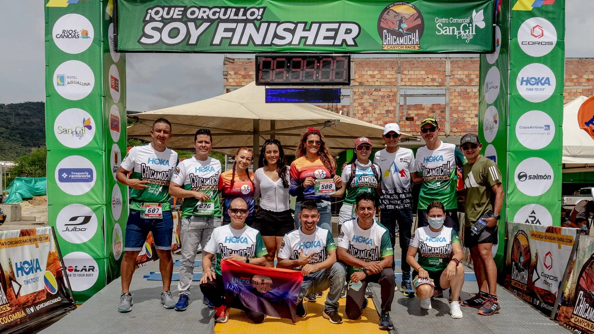 Group of finishers in race shirts posing on the "Proud to be a finisher" podium at the finish