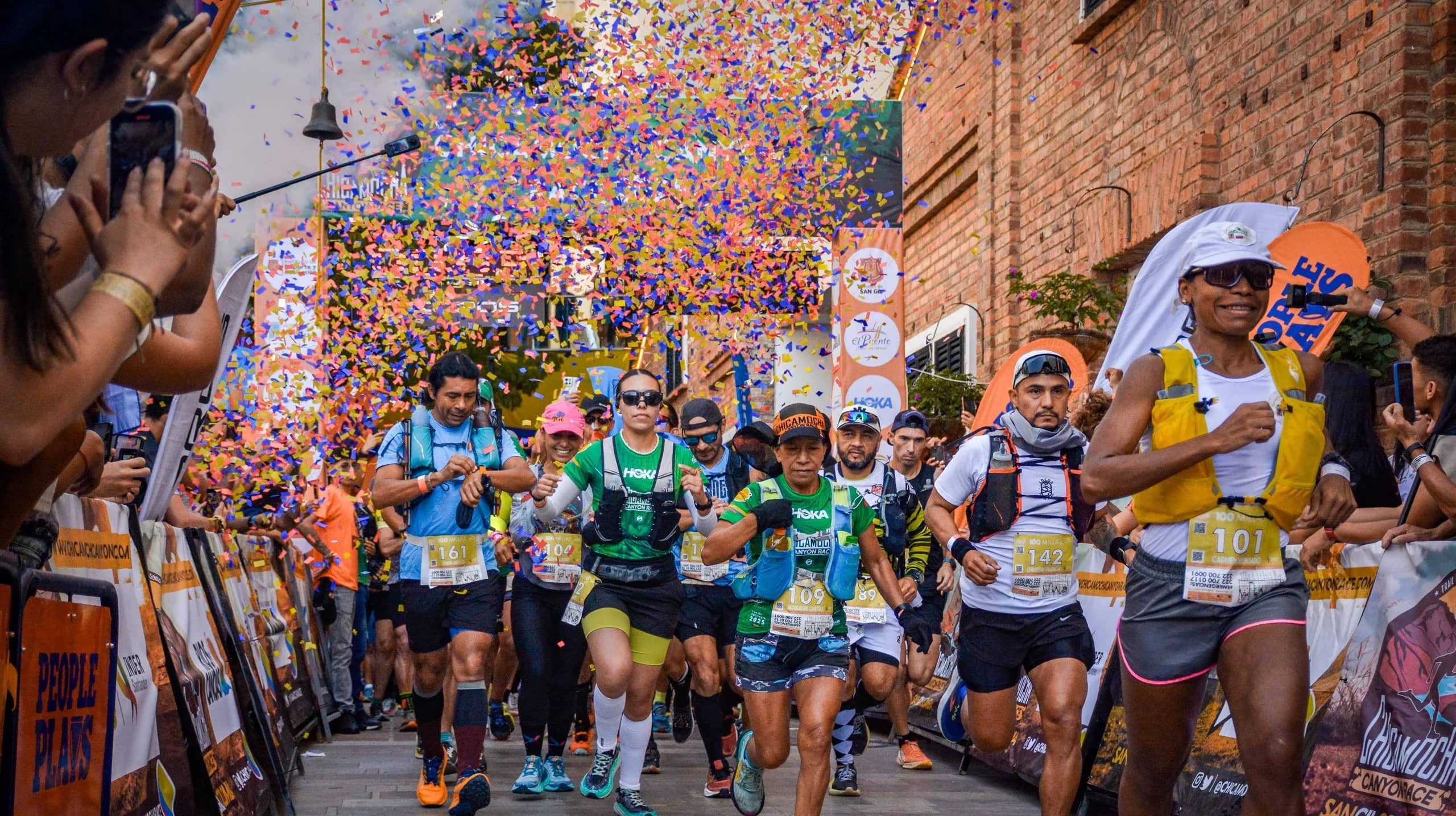 Runners starting under a shower of colorful confetti, cheered on by spectators lining the street