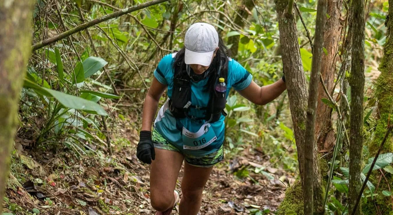 Runner in a white cap moving along a trail inside the forest on the hill