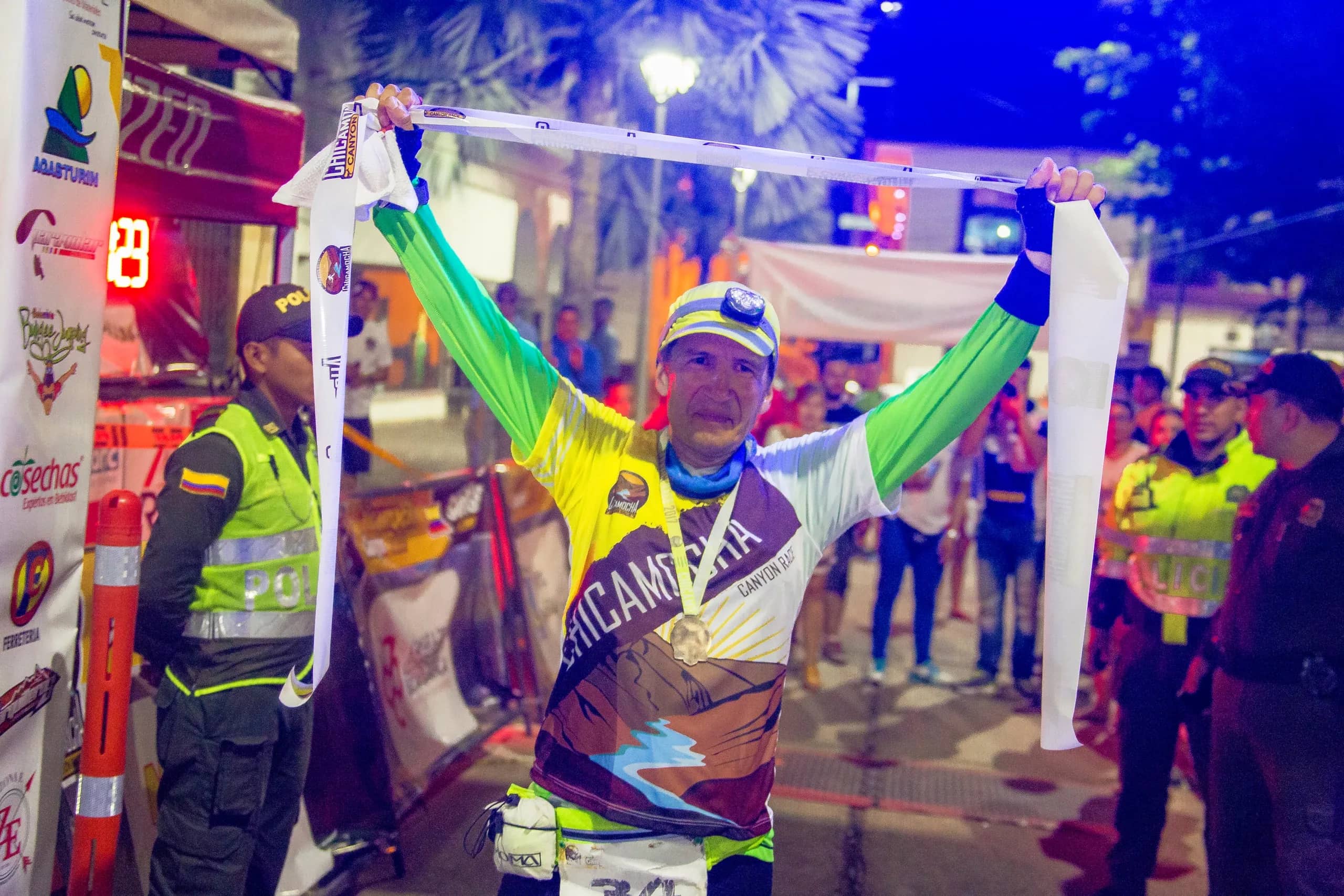 Finisher raising the finish tape at night, medal around his neck