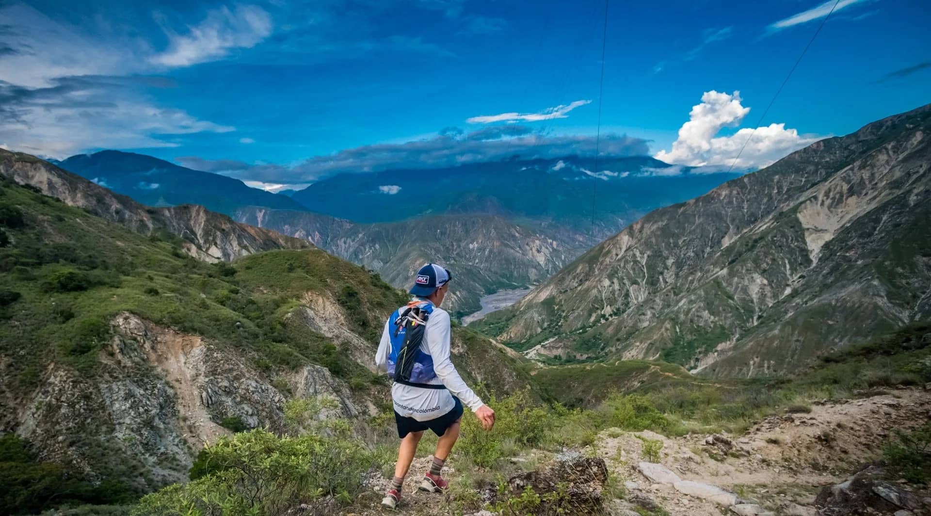 Runner descending a slope toward the canyon floor under a blue sky