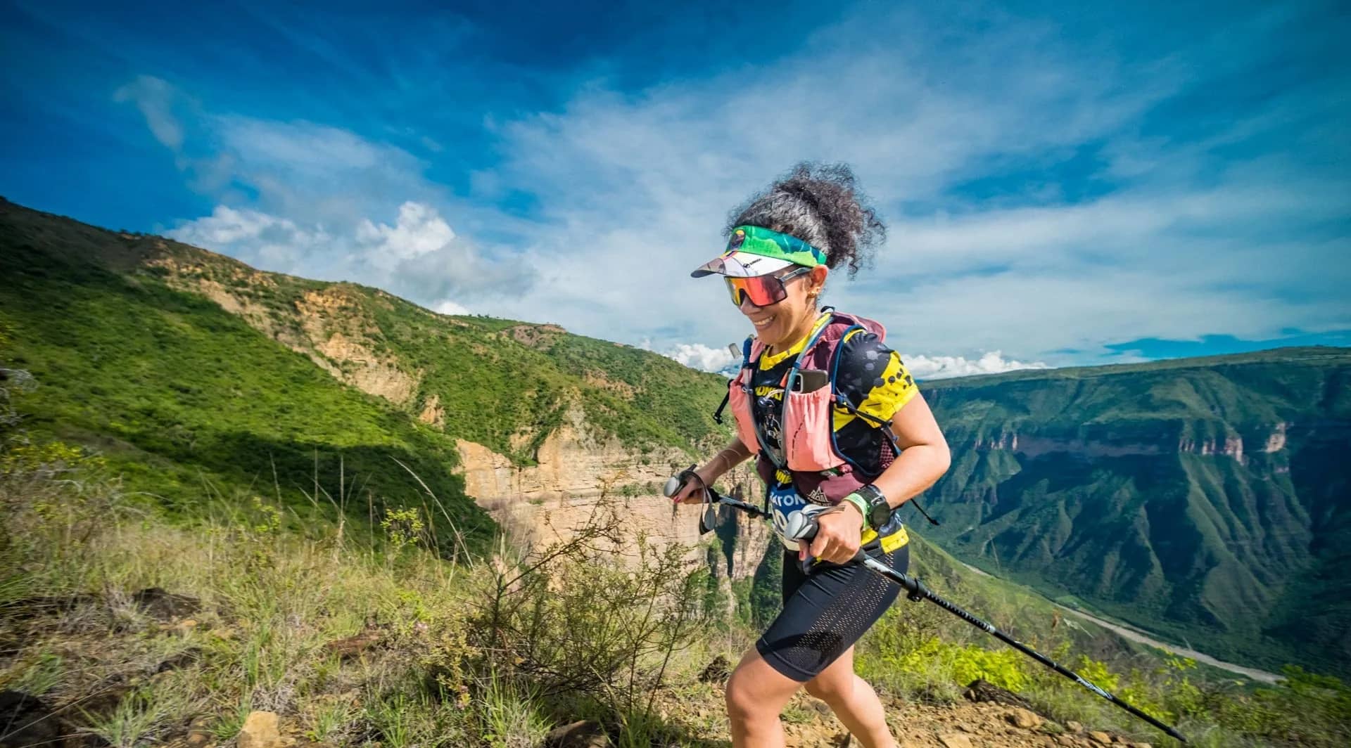 Runner with poles moves along a dirt trail with the green canyon walls behind her