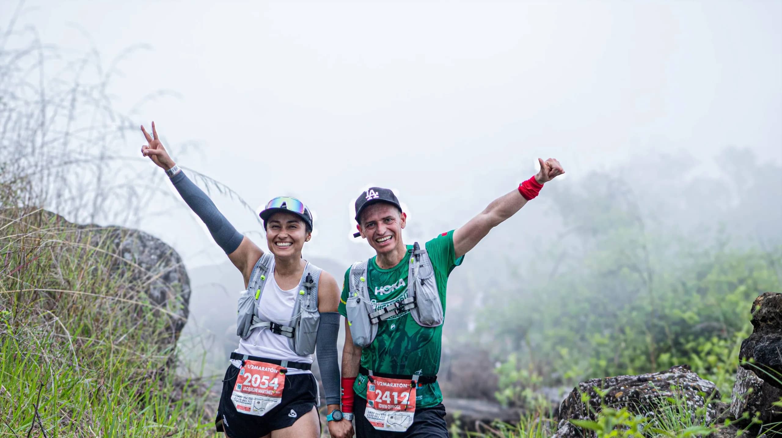 Two runners smiling with their arms raised on a misty trail